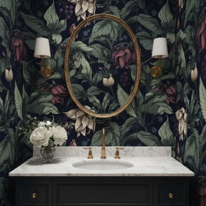May include: A bathroom vanity with a dark navy blue cabinet, white marble countertop, and gold fixtures. The oval mirror is framed in gold, and the wallpaper features a dark floral pattern with green leaves and pink and cream flowers. Two sconces with white shades flank the mirror.