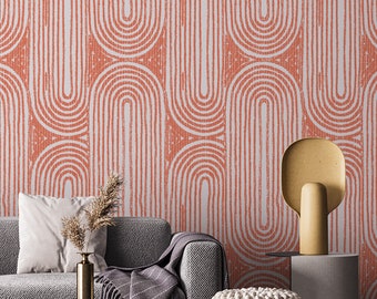May include: A room interior featuring a patterned wallpaper with a repeating arch design in coral and white. A gray sofa with a white pillow and a gold-colored lamp on a side table are in the foreground. A vase with dried plants is on the table.