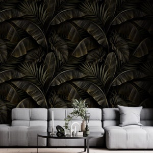 May include: Dark wallpaper featuring a repeating pattern of stylized banana leaves and other tropical foliage in shades of black and gold. The leaves have detailed veining. A gray sofa and coffee table are in the foreground.