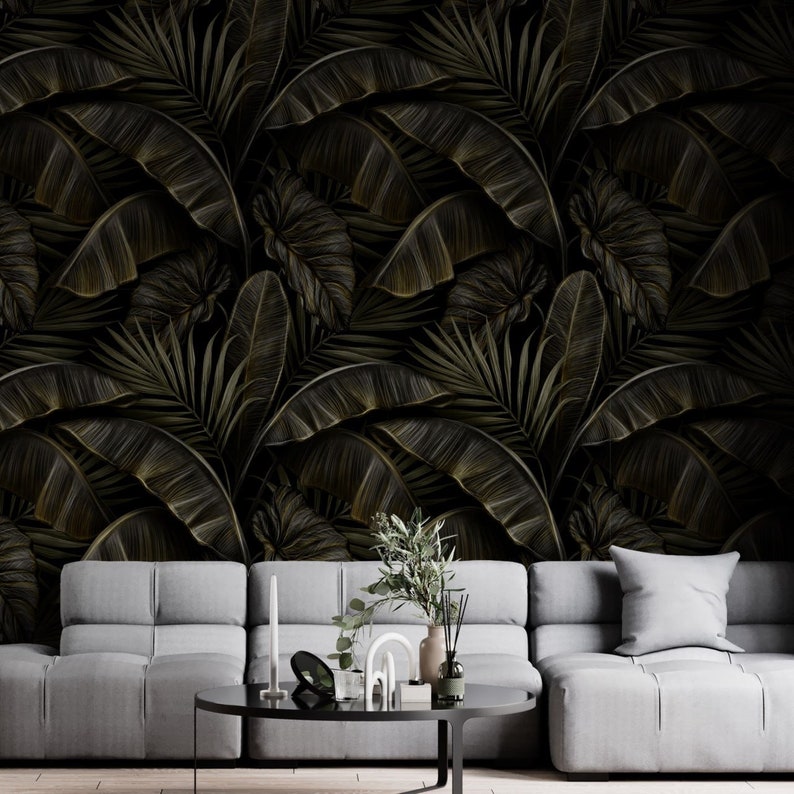 May include: Dark wallpaper featuring a repeating pattern of stylized banana leaves and other tropical foliage in shades of black and gold. The leaves have detailed veining. A gray sofa and coffee table are in the foreground.