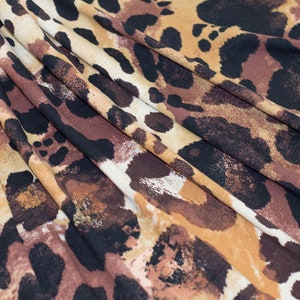 May include: Close-up of a fabric with a leopard print pattern. The fabric features a mix of brown, black, and tan spots and patches. The material is folded, creating a textured appearance with shadows and highlights.