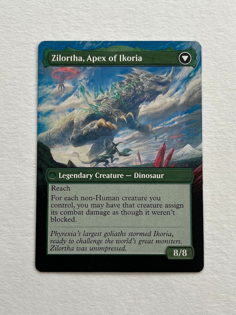 May include: A green and black Magic: The Gathering card featuring a large, green dinosaur creature with a blue background. The card is titled "Zilortha, Apex of Ikoria" and has the text "Legendary Creature - Dinosaur" and "Reach". The card has a power and toughness of 8/8.