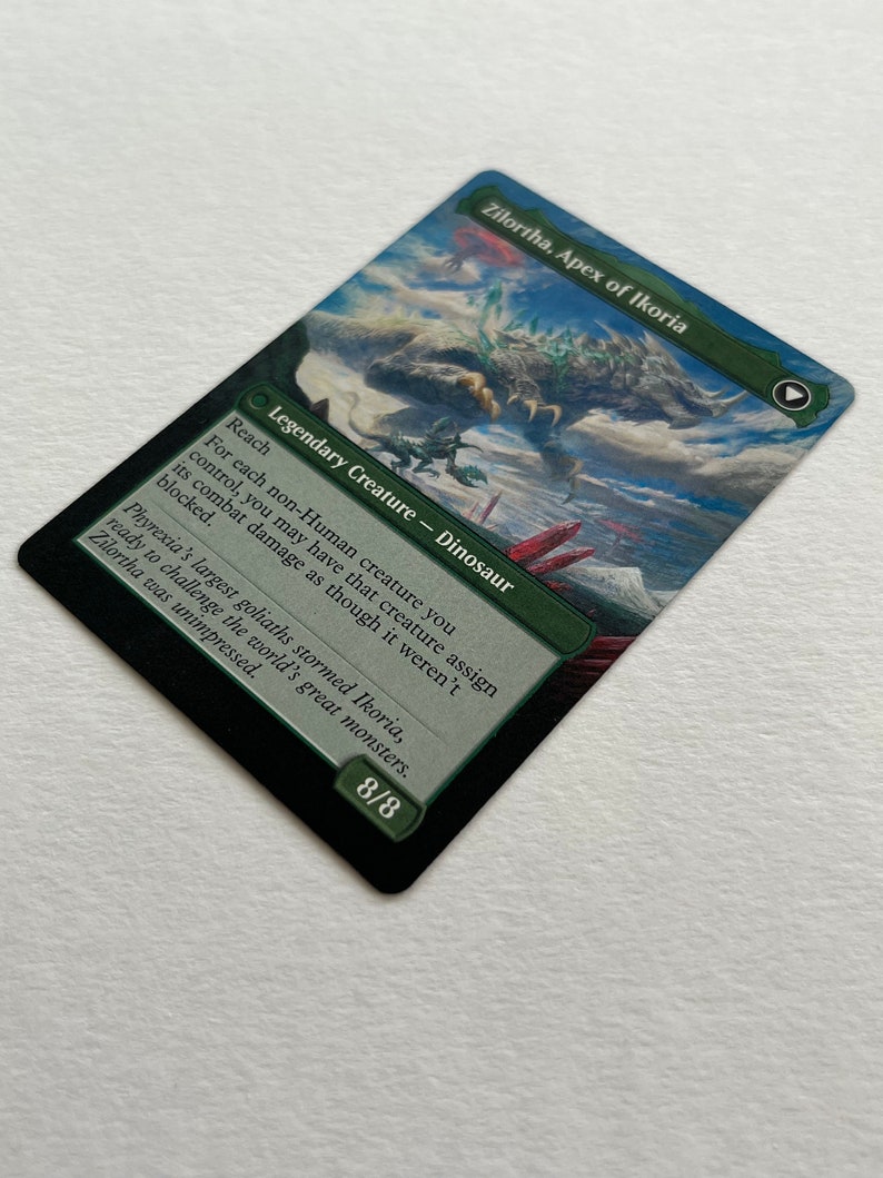 May include: A green, blue, and white fantasy art card depicting a large, green, dinosaur-like creature with a long neck and tail. The card is titled "Zilortha, Apex of Ikoria" and has the text "Legendary Creature - Dinosaur" and "Reach" on it. The card is from the Magic: The Gathering trading card game.