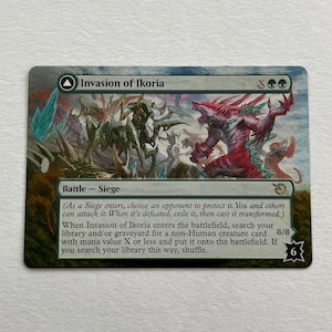 May include: A green, blue, and red fantasy creature card with the text "Invasion of Ikoria" and "Battle - Siege". The card has a green, blue, and red background with a white border. The card has a white border and a black symbol in the bottom right corner.