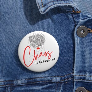 May include: White button with a black and gray line drawing of a woman with a messy bun and red lips. The text "Chaos Coordinator" is written in black below the drawing.