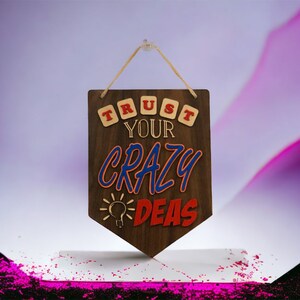 May include: Wooden sign with the text "TRUST YOUR CRAZY IDEAS" in red, blue, and yellow letters. The sign is brown and has a light bulb graphic.
