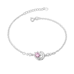 Può includere: Un braccialetto d'argento con un ciondolo a forma di luna crescente e un ciondolo a forma di sole con una pietra preziosa rosa. Il braccialetto ha una catena delicata e una chiusura a moschettone.