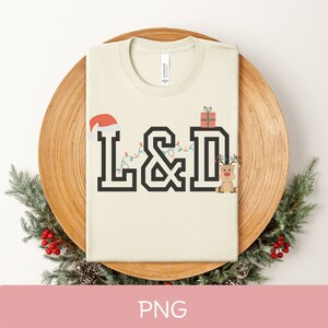 K&ouml;nnte beinhalten: Ein beiges T-Shirt mit einem schwarzen Grafikdesign der Buchstaben "L&D", verziert mit Weihnachtslichtern, einer Weihnachtsm&uuml;tze, einem Geschenk und einem Rentier. Die Buchstaben sind in einer fetten, Blockschrift.