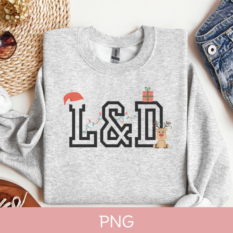 K&ouml;nnte beinhalten: Ein grauer Pullover mit einem weihnachtlichen Design, das die Buchstaben "L&D" mit einem Weihnachtsmann-Hut, Weihnachtslichtern, einer Geschenkbox und einem Rentier zeigt.