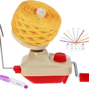 May include: A beige and red yarn ball winder with a large yellow yarn cake mounted on top. The device features a metal guide arm and a red hand crank. Included are several colorful plastic yarn needles and stitch markers, plus a small purple seam ripper with the text Ayasee printed on the handle.
