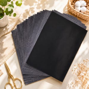 May include: A stack of rectangular black paper sheets arranged in a fan shape. The paper has a dark, solid matte finish and a smooth texture. The sheets are layered neatly, creating a uniform appearance with sharp edges and a consistent dark color.
