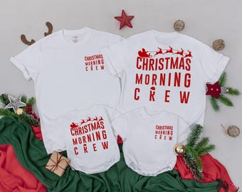 Könnte beinhalten: Weiße T-Shirts und ein Body mit dem Text "Christmas Morning Crew" in Rot. Ein Shirt zeigt den Weihnachtsmann und Rentiere. Festliche Urlaubsbekleidung für die ganze Familie.