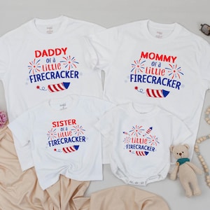 May include: White t-shirts with red, white, and blue text and firework graphics. The shirts say "Daddy of a little Firecracker", "Mommy of a little Firecracker", "Sister of a little Firecracker", and "Little Firecracker".