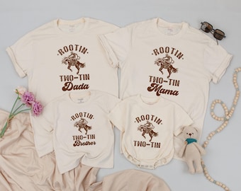 May include: A set of four cream-colored t-shirts with a brown cowboy riding a horse graphic and the text "Rootin' Two-Tin" with the words "Dada", "Mama", "Brother", and "" printed below the graphic.