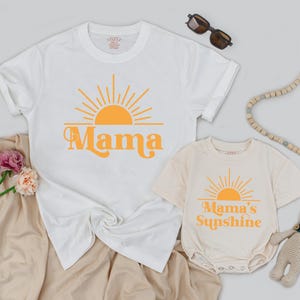 May include: Two white t-shirts with a yellow sun graphic. The larger shirt says "Mama" and the smaller shirt says "Mama's Sunshine".