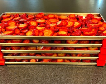 Könnte beinhalten: Fünf übereinander gestapelte Edelstahlschalen, die jeweils mit geschnittenen Erdbeeren gefüllt sind. Die Schalen haben rote Plastikclips an den Ecken.