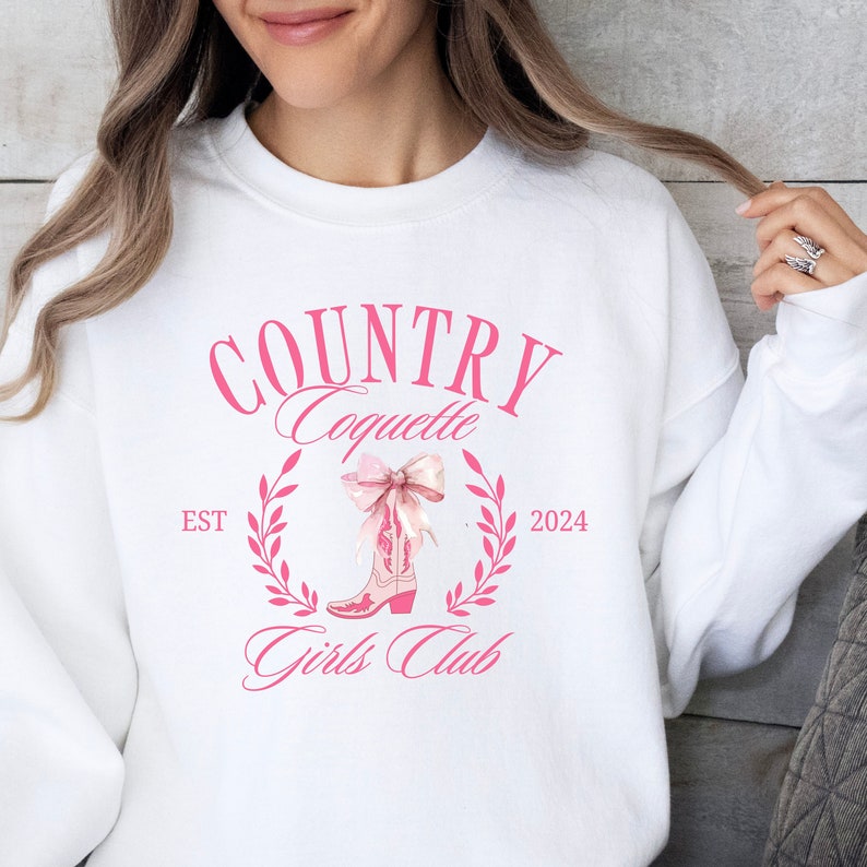 May include: White sweatshirt with a pink graphic design that says "COUNTRY Coquette Girls Club" with a pink boot and bow in the centre. The text "EST 2024" is on either side of the boot.