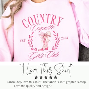 May include: Pink sweatshirt featuring a graphic design of pink cowboy boots with a bow, a wreath of leaves, and the text "COUNTRY Coquette EST 2024 Girls Club". The text "I Love This Shirt" is written below the graphic.