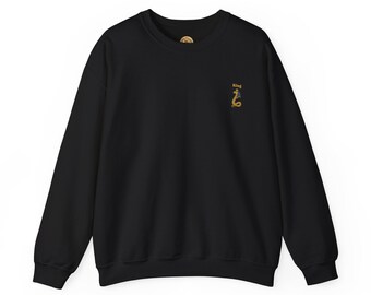 May include: Black crewneck sweatshirt with a small embroidered design of a snake wearing a crown, with the word "King" above it. The design is in gold, blue, and black. The sweatshirt has a round neck and long sleeves.