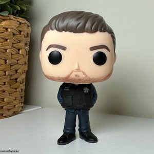 May include: A vinyl figure of a man wearing a dark blue uniform with a badge on the chest. He has brown hair and a beard. The figure has a large head and small body, typical of a Funko Pop figure.