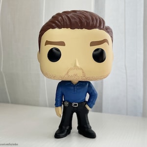 May include: A custom-painted Funko Pop figure of a man with brown hair, a blue shirt, black pants, and a black belt. The figure has a realistic paint job and is posed with one hand on his hip.