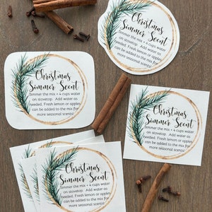 May include: Four white square cards with a gold circle and a green pine branch design. The text on the cards reads "Christmas Simmer Scent" and includes instructions for simmering the mix with 4 cups of water on the stovetop.  Add water as needed. Fresh lemon or apples can be added to the mix for more seasonal scents!"