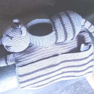Pode incluir: Um organizador em forma de gato de crochê feito à mão em tons de cinza e cinza escuro. O gato tem uma cabeça, um corpo em forma de cesta, um bolso e uma cauda longa. Um pequeno telefone está no bolso.