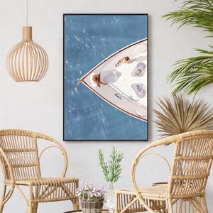 May include: An aerial view of a white sailboat with people on board, floating on a blue body of water. The boat is in the center of the image, with the bow facing the viewer. The water is a light blue color, and the sky is a clear blue.