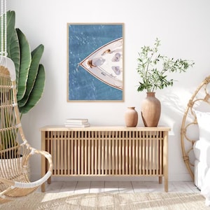May include: A framed photograph of a white boat on the water. The boat is viewed from above, and the bow of the boat is facing the viewer. The water is a light blue color, and the sky is a light blue color. The photograph is hanging on a white wall.