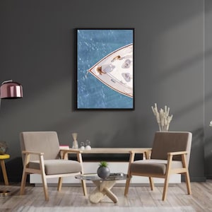 May include: A photograph of a white sailboat with a wooden bow, viewed from above, floating on a blue body of water. The boat is surrounded by blue water with whitecaps.
