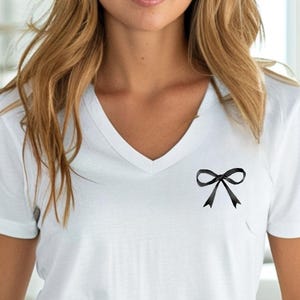 May include: A white v-neck t-shirt with a black bow on the front.
