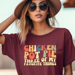 May include: A maroon t-shirt with a retro-style graphic that reads "Chicken Pot Pie Three of My Favorite Things".