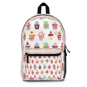 May include: White backpack with a repeating pattern of colorful cupcakes. The cupcakes have various toppings and decorations, including hearts, cherries, and bows. The backpack has a black zipper, a black handle, and a mesh side pocket.