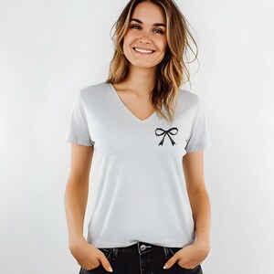 May include: A light gray v-neck t-shirt with a black bow on the left side of the chest.
