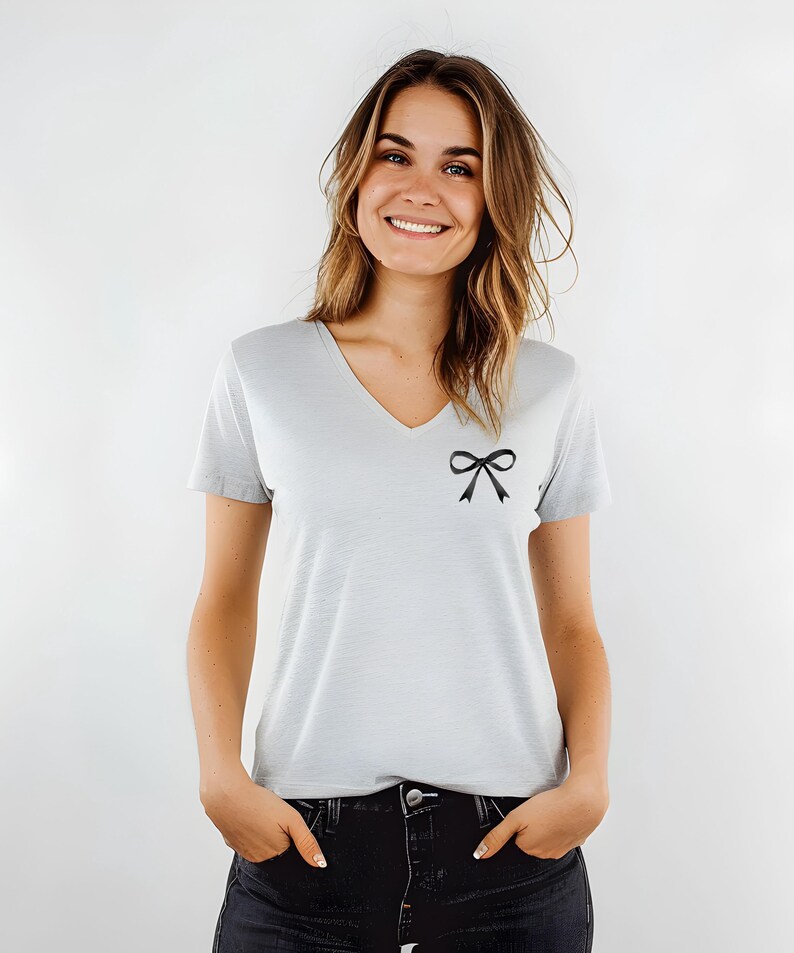 May include: A light gray v-neck t-shirt with a black bow on the left side of the chest.