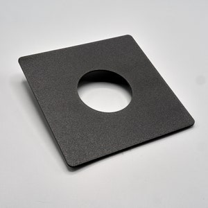 May include: A black square-shaped plate with a round hole in the center. The plate has a textured surface.