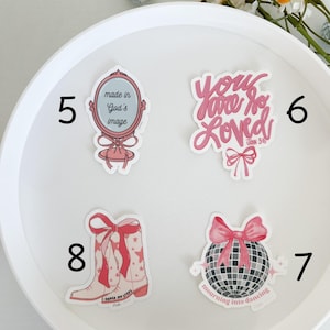 May include: A set of eight pink and white stickers with various designs and inspirational messages. The stickers include a mirror with the text "made in God's image", a disco ball with the text "mourning into dancing", a pair of cowboy boots with the text "order my steps", and a heart with the text "you are so loved John 3:16".