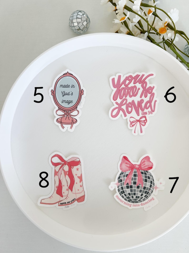 May include: A set of eight pink and white stickers with various designs and inspirational messages. The stickers include a mirror with the text "made in God's image", a disco ball with the text "mourning into dancing", a pair of cowboy boots with the text "order my steps", and a heart with the text "you are so loved John 3:16".