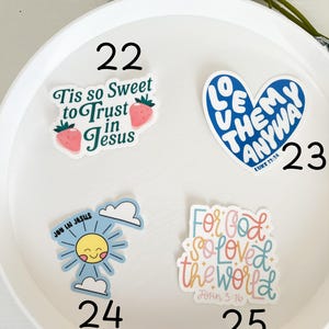 May include: A white plate with four colorful stickers with religious quotes. The stickers are numbered 22, 23, 24, and 25. The stickers feature a strawberry, a heart, a sun, and a hand-drawn font.