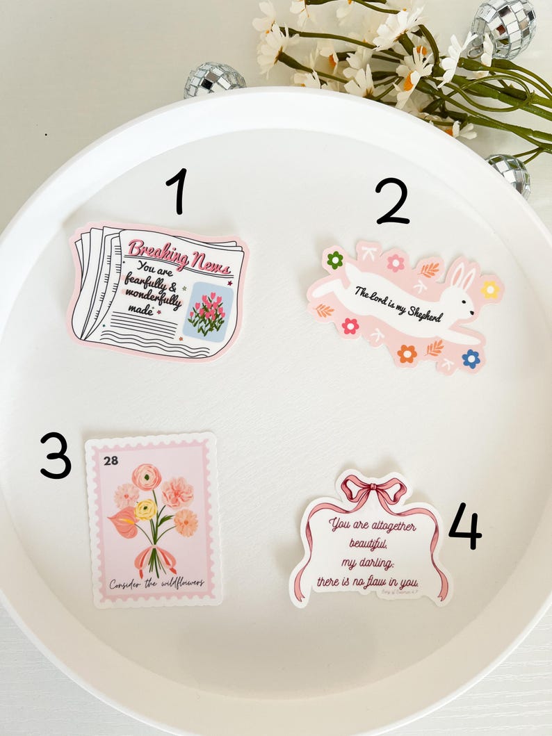 May include: Four pink and white stickers with inspirational quotes and illustrations. The first sticker says "Breaking News: You are fearfully and wonderfully made." The second sticker has a bunny with the quote "The Lord is my Shepherd." The third sticker has a bouquet of flowers with the quote "Consider the wildflowers." The fourth sticker has a pink ribbon with the quote "You are altogether beautiful my darling: there is no flaw in you."