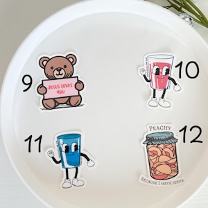 May include: Four stickers on a white background. The stickers are numbered 9, 10, 11, and 12. The stickers feature a brown teddy bear holding a sign that says "Jesus Loves You", a pink cartoon glass of juice, a blue cartoon glass of water, and a jar of peaches with the text "Peachy Because I Have Jesus".