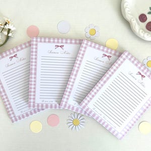 May include: Four pink and white gingham notepad sets with the words "Sermon Notes" printed on the front. Each notepad has a pink bow and the words "Be sure of the Word and be sure of your memory".