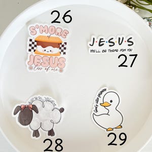 May include: Four stickers on a white background. The stickers are round and feature various designs. One sticker features a s'more with the text "S'more Jesus" and "Less of me". Another sticker features the text "J.E.S.U.S." with the text "He'll be there for you". The third sticker features a white duck with the text "God's little follower". The fourth sticker features a white sheep with a pink bow and the text "You left the 99 to follow me".