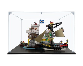 May include: A white Lego castle with a black ship docked at the side. The castle has a red door and a black cannon. The ship has a brown sail and a black mast. The set is displayed in a clear acrylic display case with a black base.