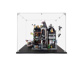 May include: A detailed Lego set of a building with multiple levels, featuring a dark color scheme and various minifigures. The set is enclosed in a clear display case with a black base, showcasing the intricate design and characters.