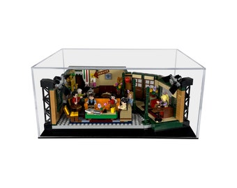 May include: A clear acrylic display case with a black base, showcasing a LEGO Friends Central Perk set. The set features the iconic orange couch, a coffee table, and minifigures of the six main characters from the TV show.