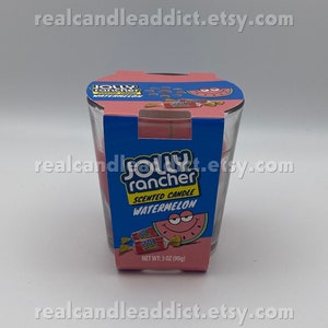 May include: A Jolly Rancher scented candle in a glass jar with a watermelon design. The candle is pink and has a net weight of 3 ounces (90 grams).
