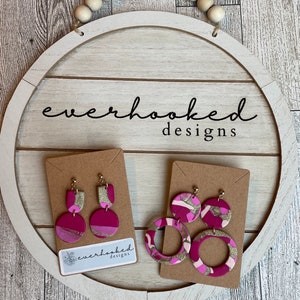 Op de afbeelding: Twee paar roze en gouden oorbellen met een geometrisch ontwerp. De oorbellen worden gepresenteerd op een kaart met de tekst "everhooked designs".