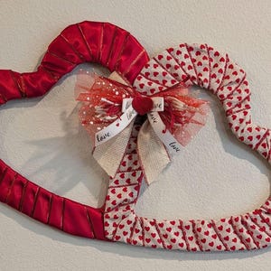 May include: A red and white heart-shaped wreath with a burlap bow and the word "love" written on the ribbon. The wreath is decorated with small red hearts.