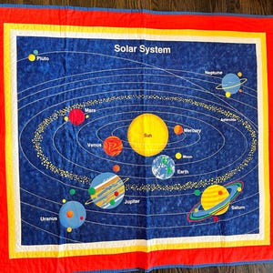 Puede incluir: Una colcha de tela cuadrada con un fondo azul oscuro de temática espacial y el texto Solar System. Muestra el Sol, los planetas y un cinturón de asteroides con líneas orbitales blancas. La colcha tiene un borde amarillo y rojo con ribete azul.